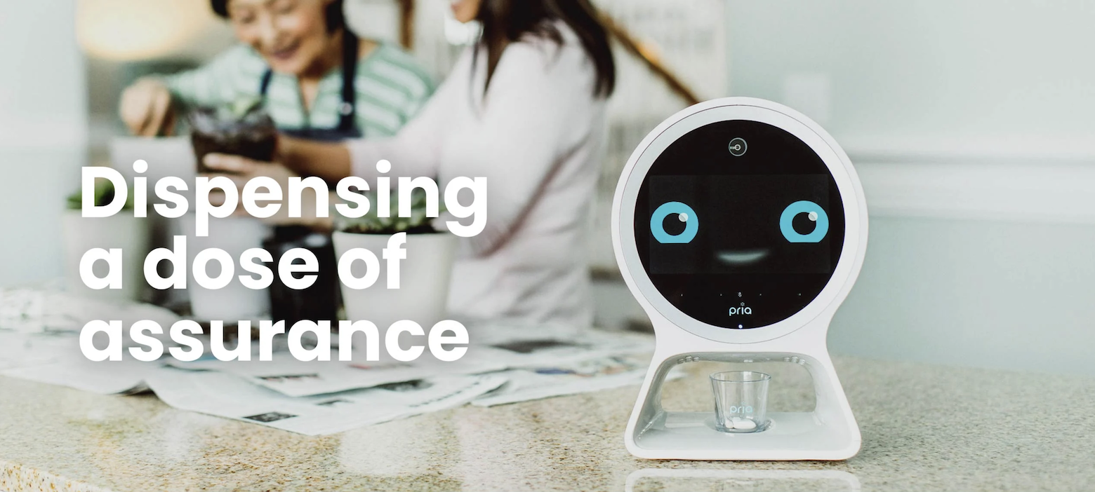 The pill dispenser Pria has a round screen with eyes and a smile to reassure patients. Below its screen, it dispenses pills into a cup.