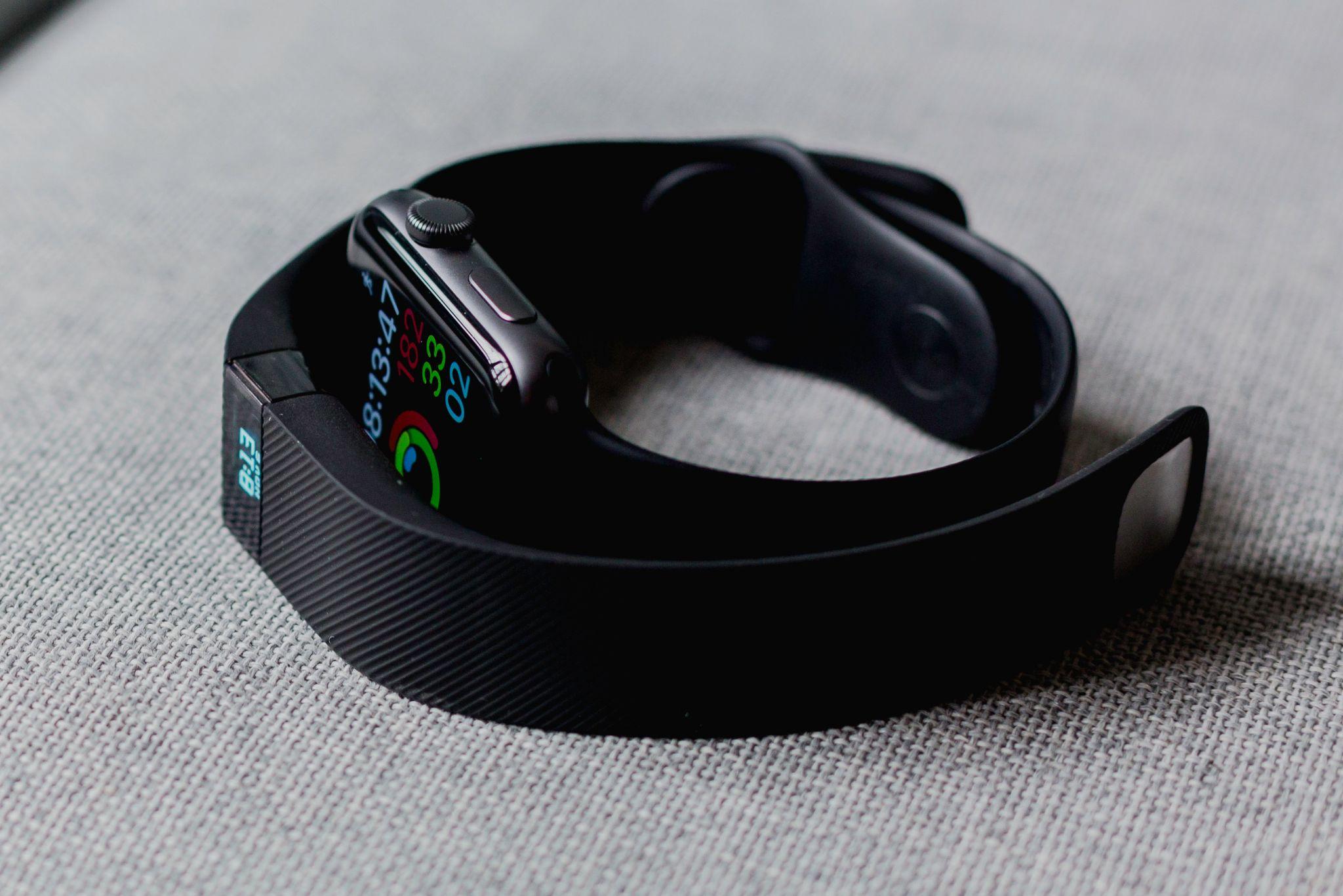 A Fitbit and an Apple watch on a gray fabric background.