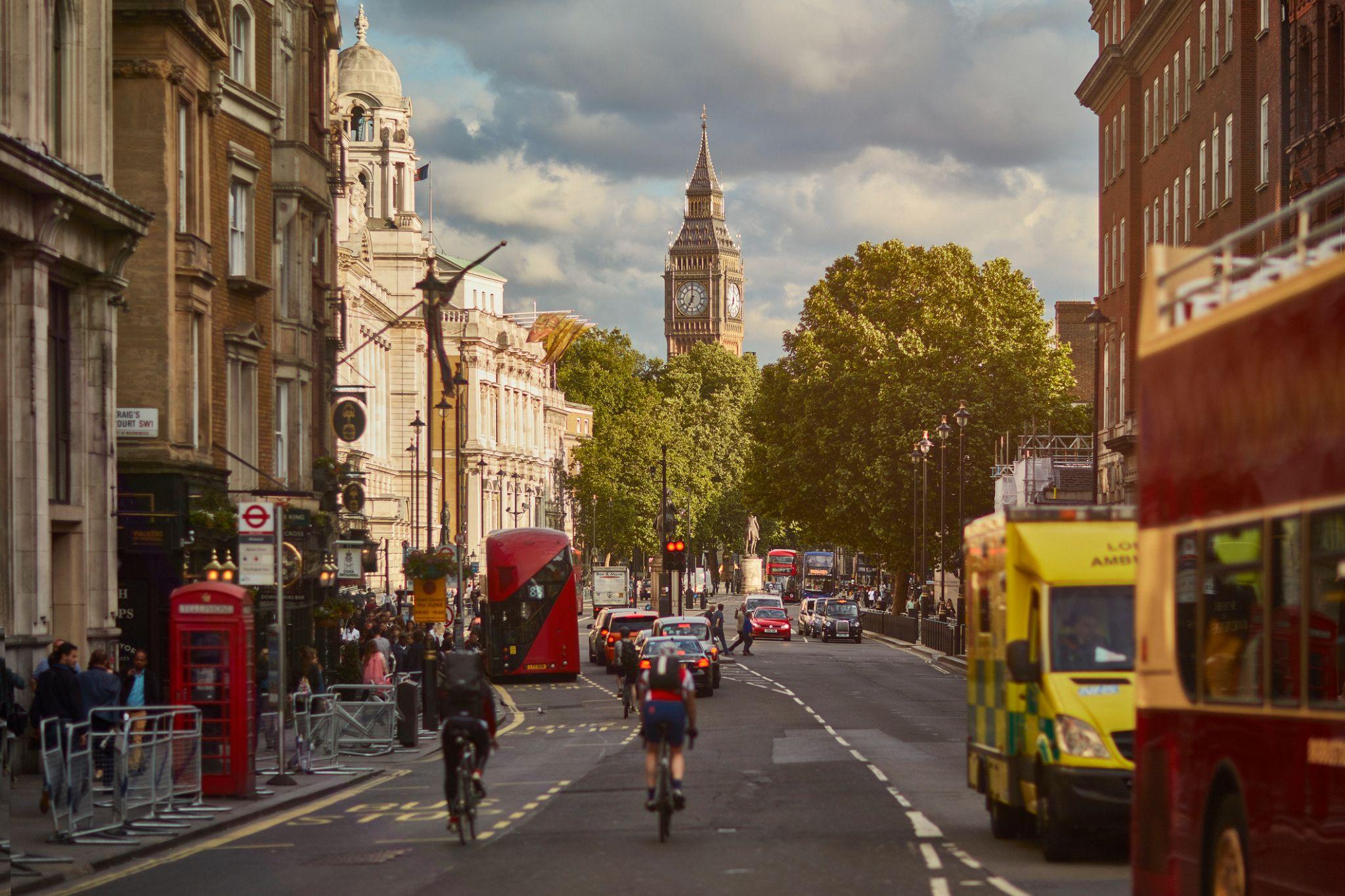 This photo shows two people on bicycles wearing large backpacks as they ride down a London street.