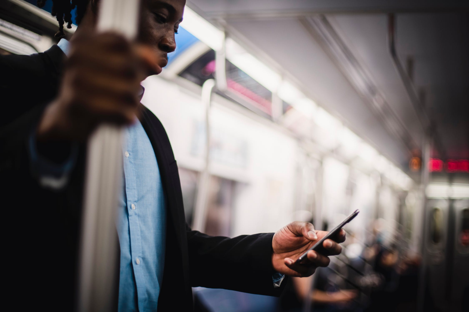 Photo of a man holding a subway pole with one hand and a mobile phone in the other. One of the most important mobile UX best practices is ensuring important features continue to work even with little or no internet connectivity.
