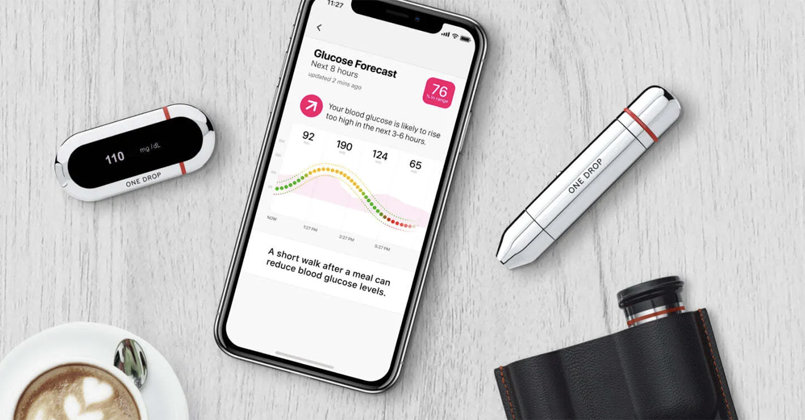 A One Drop glucose meter, chrome lancer, and carrying pouch surrounding a smartphone displaying a glucose forecast.