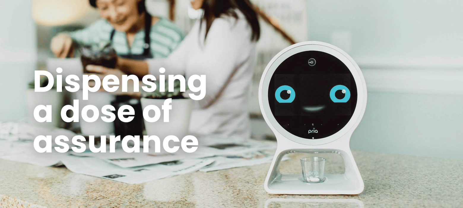 The pill dispenser Pria has a round screen with eyes and a smile to reassure patients. Below its screen, it dispenses pills into a cup.