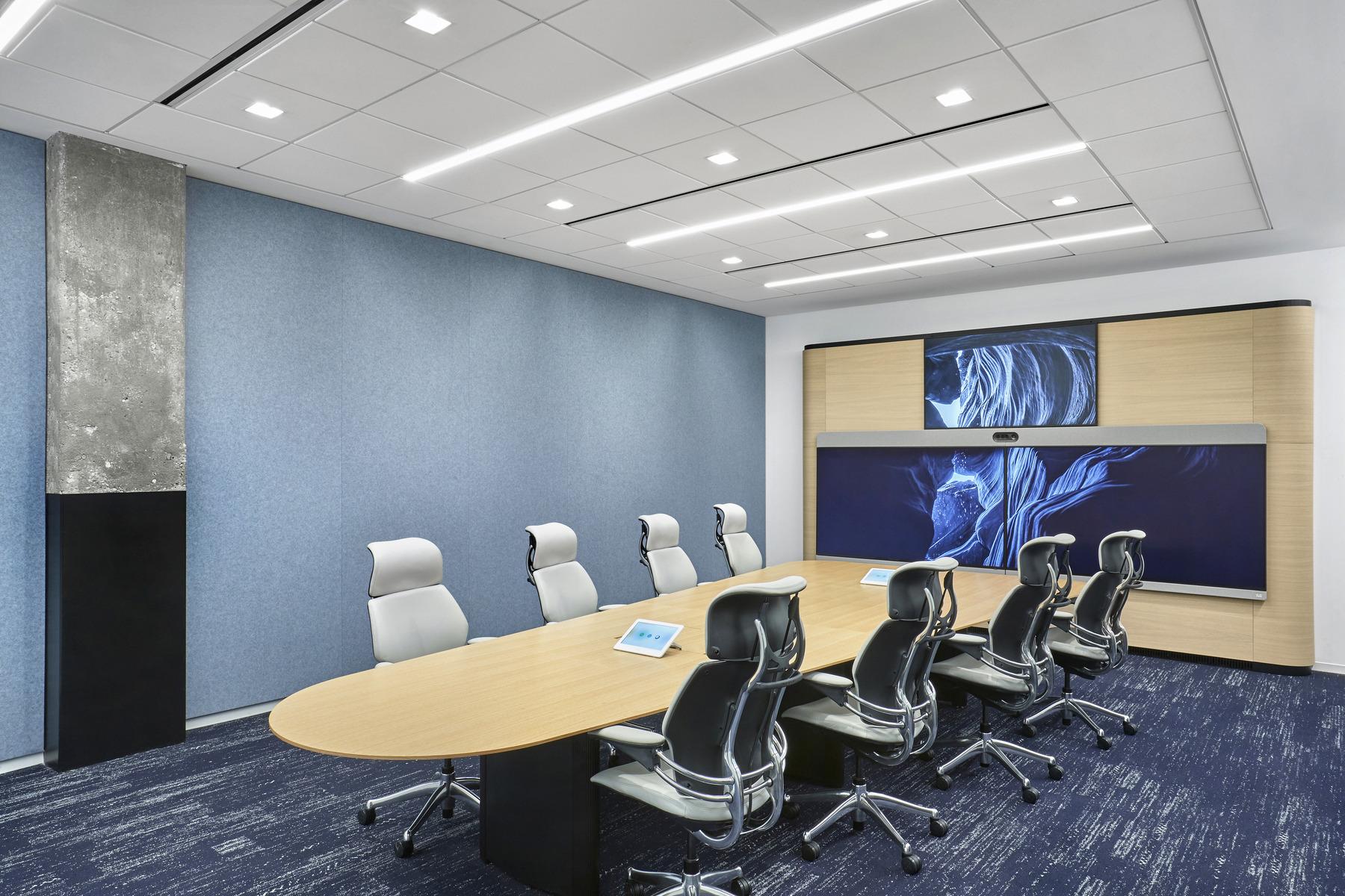 A conference room with three large screens on the wall and seating that allows everyone in the room, including people working remotely, to see each other during hybrid meetings.
