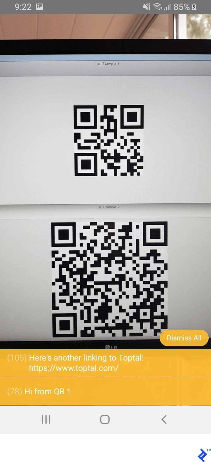 The same camera angle as before, now with console popups at the bottom having decoded the messages in the QR codes: "Hi from QR1" and Toptal's web site address.